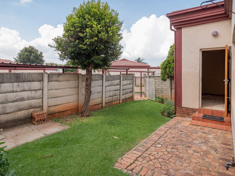 A private rear garden featuring a paved patio area, a well-maintained lawn, and a secure precast concrete boundary wall.