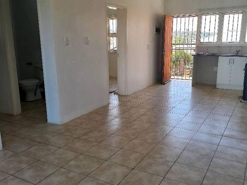 Open-plan living area featuring tiled flooring, a functional kitchen space, and direct access to an outdoor balcony area with security features.