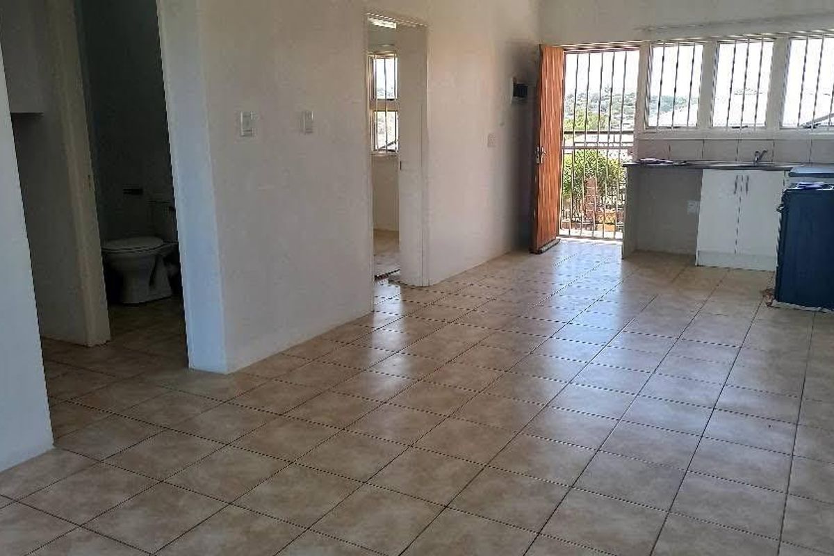Open-plan living area featuring tiled flooring, a functional kitchen space, and direct access to an outdoor balcony area with security features.