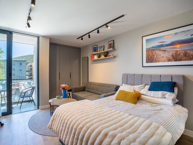 Modern bedroom featuring built-in cupboards, track lighting, and direct access to a private balcony through sliding glass doors.