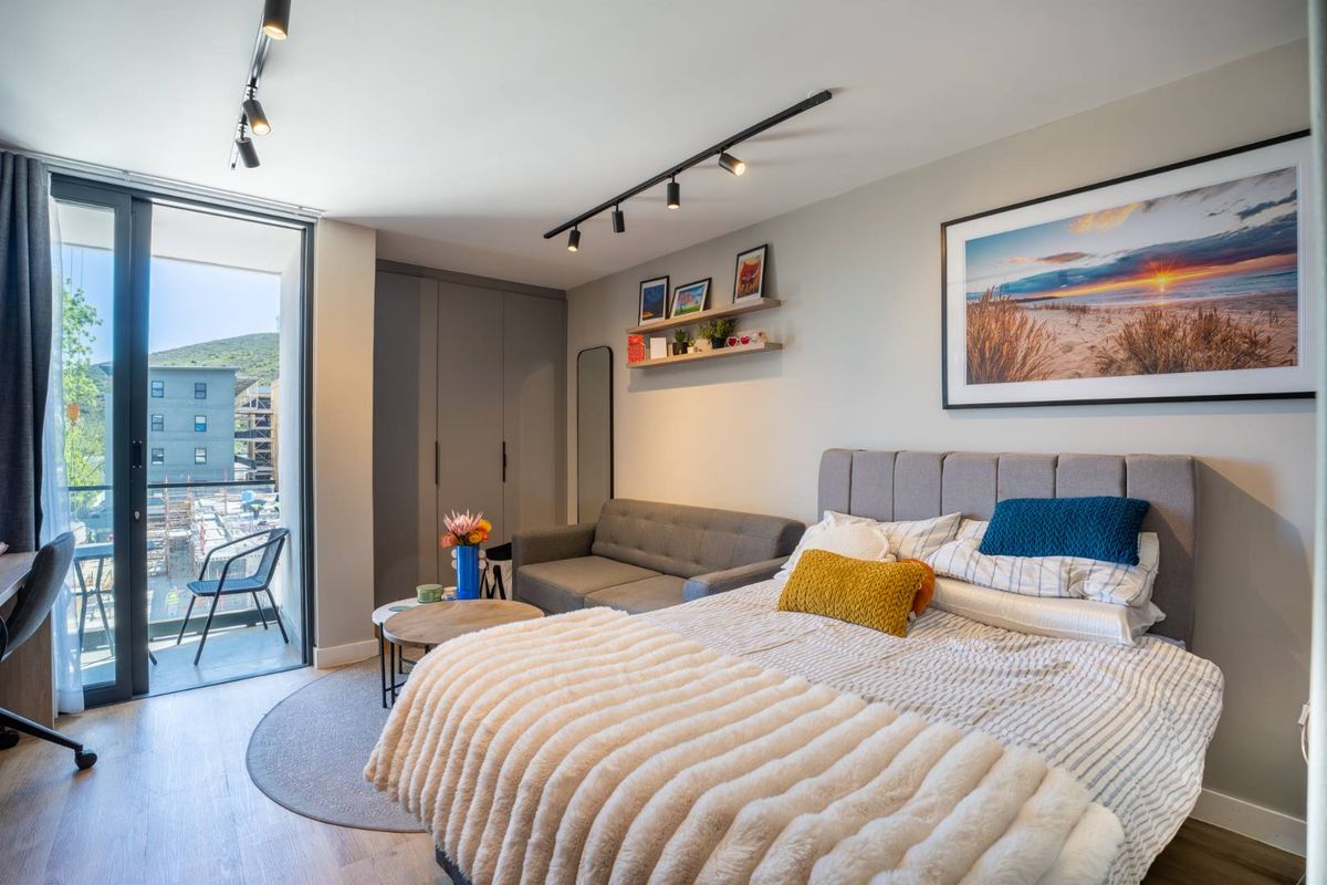 Modern bedroom featuring built-in cupboards, track lighting, and direct access to a private balcony through sliding glass doors.