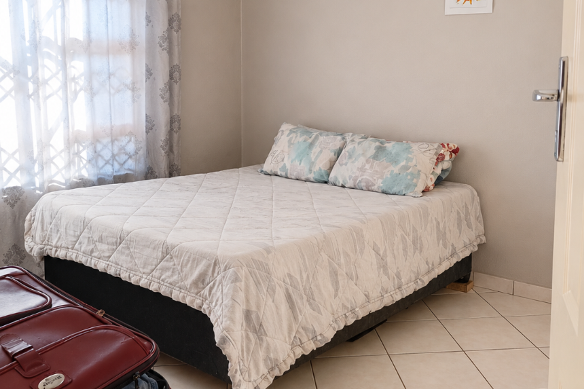 A functional bedroom featuring neutral wall tones, tiled flooring, and a window fitted with a security gate.