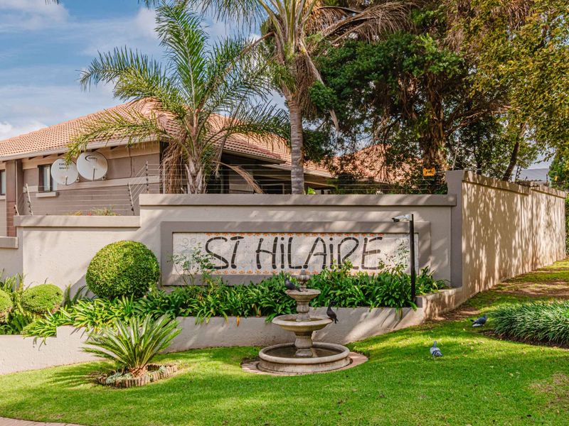 Front entrance view of St Hilaire complex featuring a landscaped garden, stone fountain, and secure perimeter wall with electric fencing.