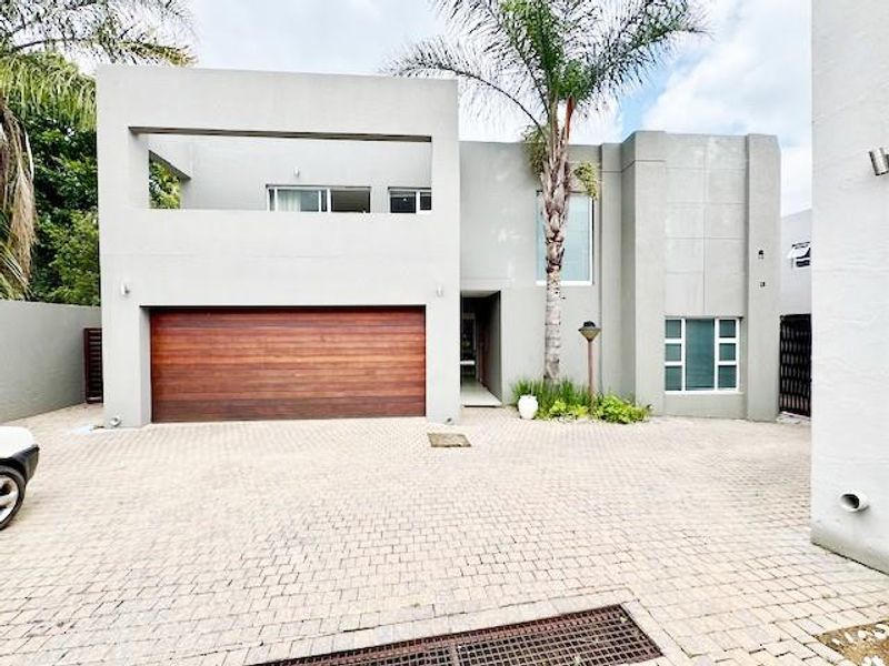 Modern double-storey cluster home featuring a paved driveway, wooden garage door, and a private balcony.