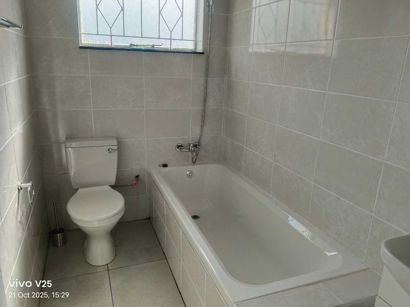 A functional bathroom featuring full-height wall tiling, a standard bathtub with a handheld shower mixer, and a white ceramic toilet.