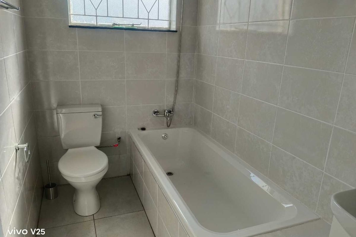 A functional bathroom featuring full-height wall tiling, a standard bathtub with a handheld shower mixer, and a white ceramic toilet.