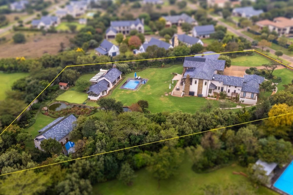 Aerial view of a large residential estate featuring multiple buildings, a swimming pool, landscaped gardens, and a putting green within a fenced boundary.