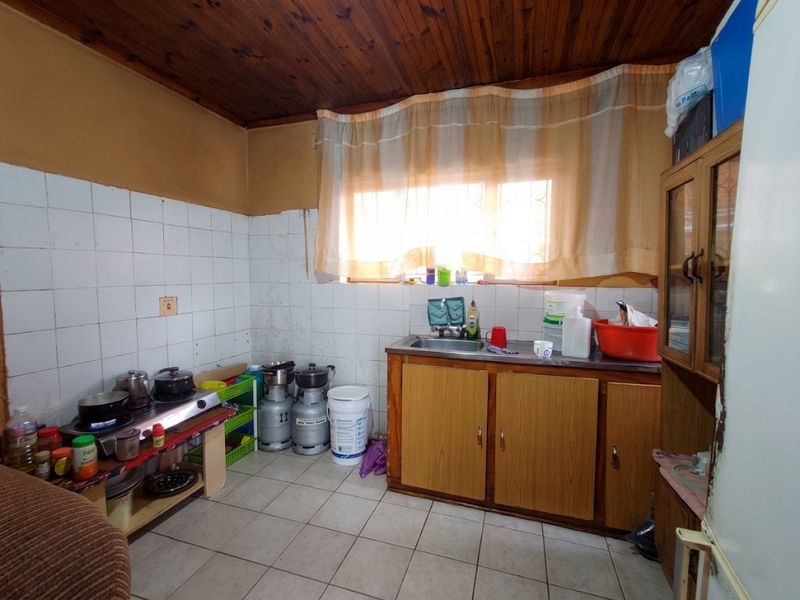 A functional kitchen featuring timber ceiling, tiled splashback, stainless steel sink, and laminate cabinetry, requiring cosmetic updates to improve its overall condition.