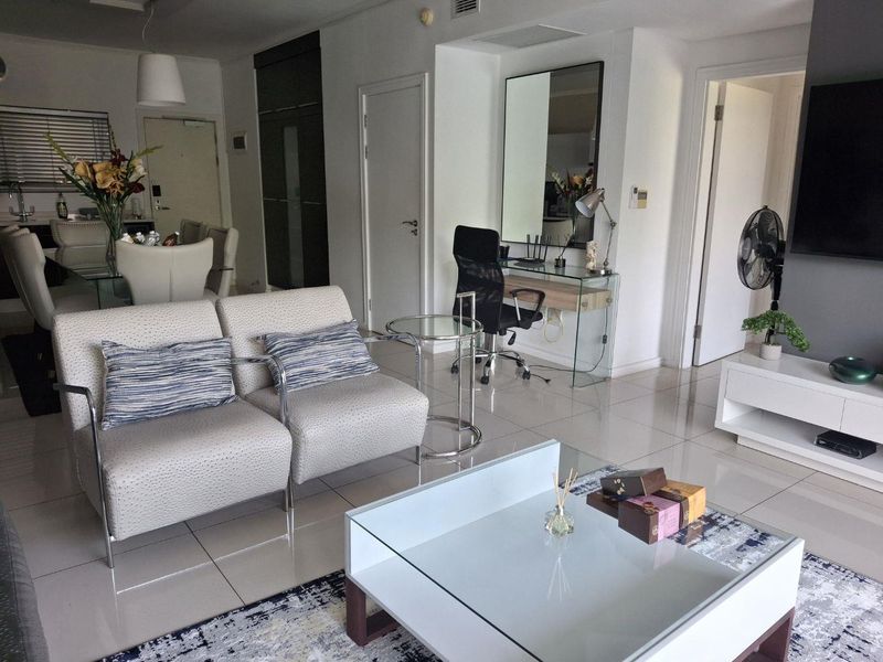 A bright open-plan living and dining area featuring polished tiled flooring, neutral walls, and integrated storage solutions, creating a functional and modern living space.