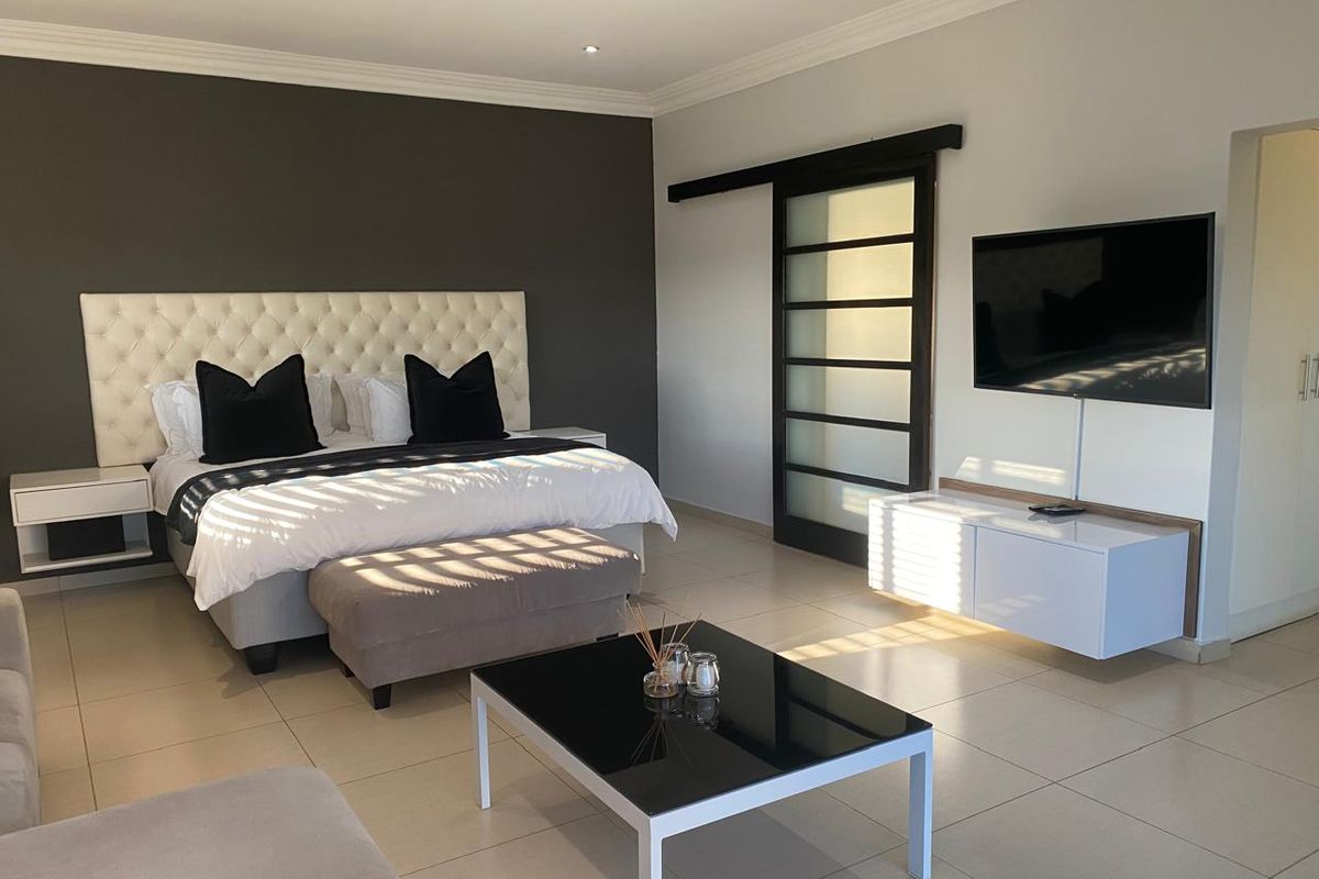 A spacious, modern bedroom featuring neutral tiled flooring, a dark accent wall, recessed lighting, and a contemporary sliding barn door.