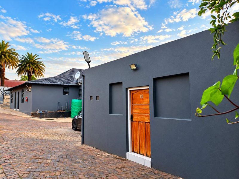 Exterior view of a modern guest house unit featuring a dark grey facade, timber entrance door, and paved driveway area.
