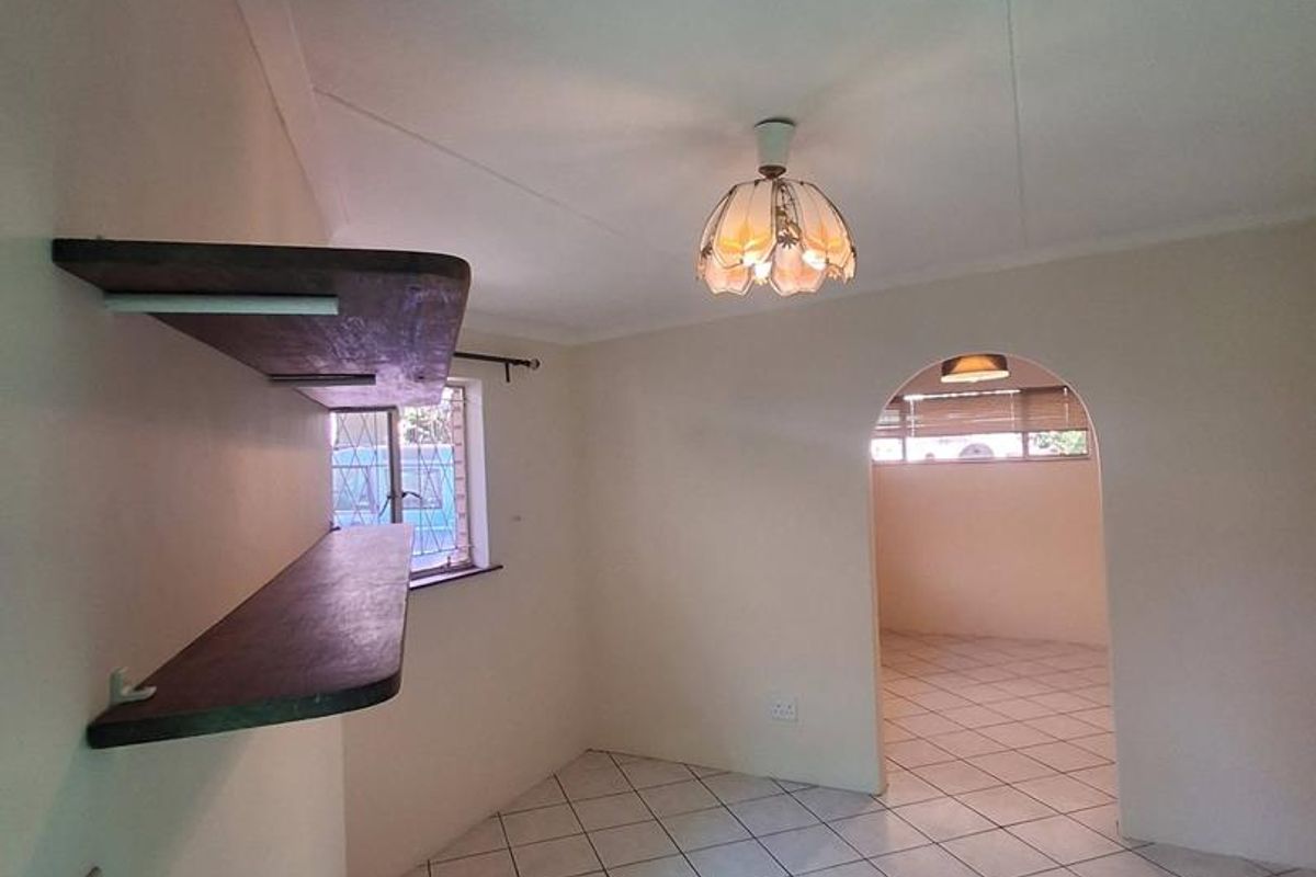 An empty living area featuring tiled flooring, an arched doorway leading to an adjacent space, and built-in wall shelving.