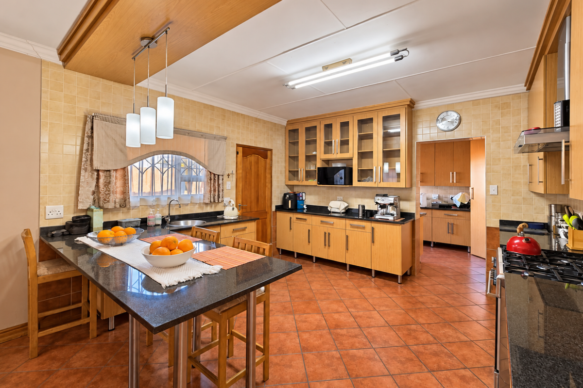 Spacious kitchen featuring wooden cabinetry, granite countertops, terracotta flooring, and an adjoining scullery area, offering a functional layout with ample storage.