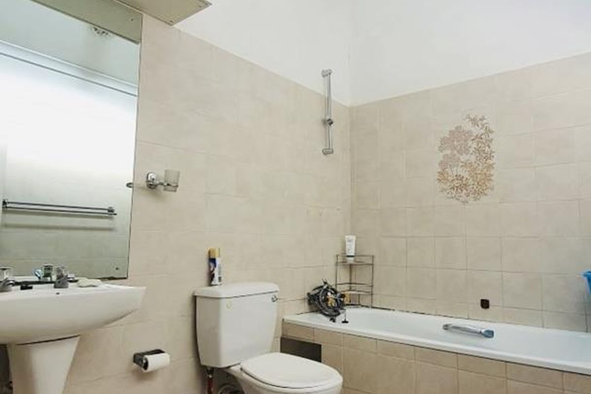 A bathroom featuring a pedestal basin, a standard bathtub with tiled surround, and a high vaulted ceiling with clerestory windows.