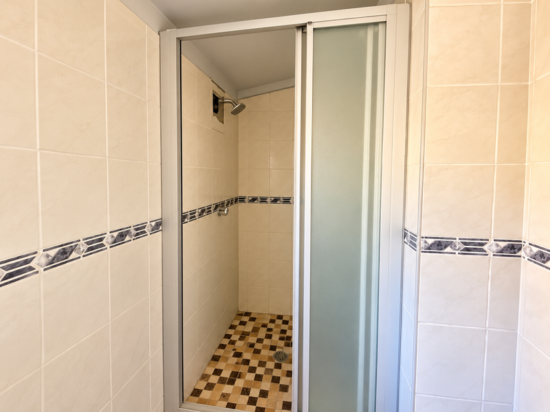 A clean, functional shower stall featuring neutral wall tiles with a decorative border and a checkered floor tile pattern.