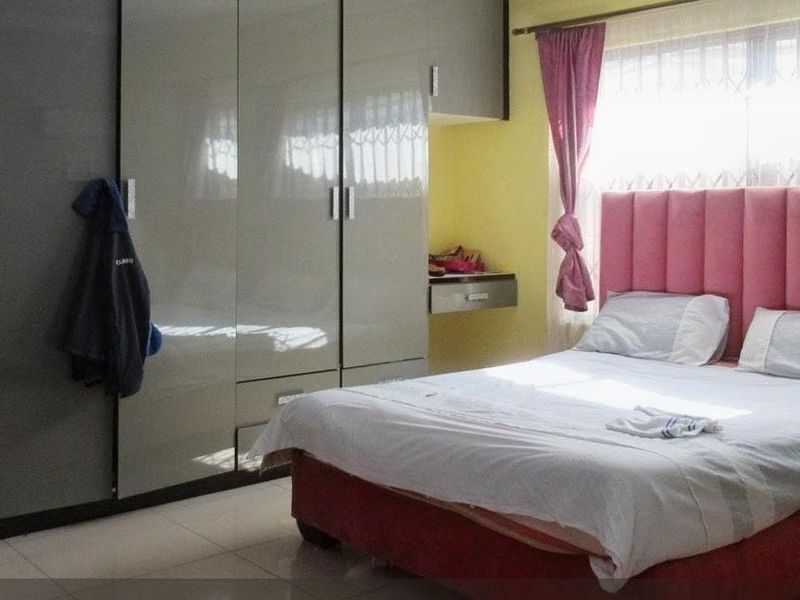 A bedroom featuring built-in cupboards, tiled flooring, and security bars on the window.