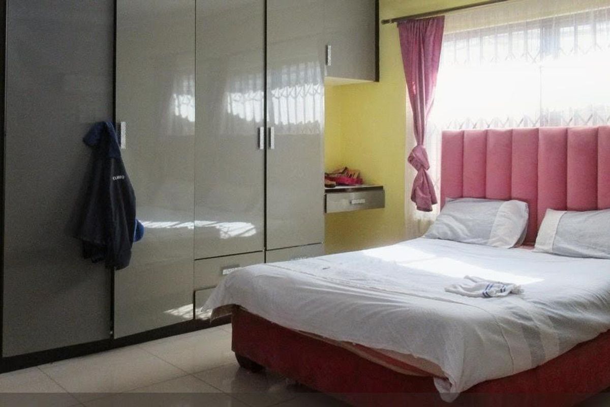 A bedroom featuring built-in cupboards, tiled flooring, and security bars on the window.