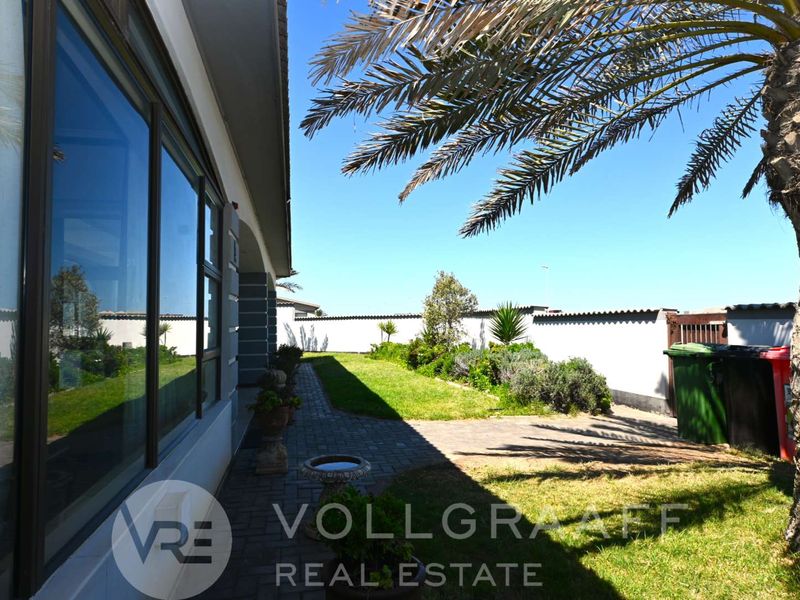 A view of the rear exterior featuring a paved walkway, landscaped garden, and large sliding glass doors leading into the home.