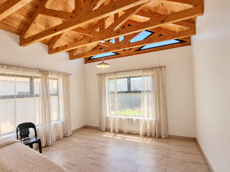 Spacious bedroom featuring high vaulted ceilings with exposed timber trusses, tiled flooring, and large windows that provide ample natural light.
