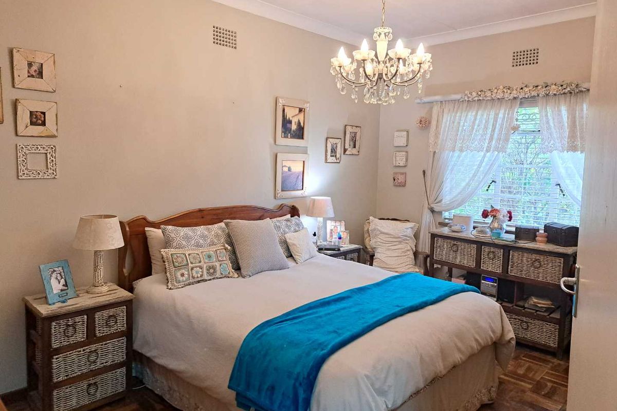 A cozy bedroom featuring parquet flooring, a decorative chandelier, and a window with natural light.