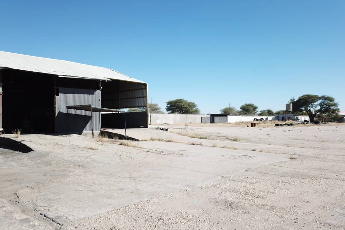 Expansive industrial yard featuring a large metal-clad warehouse structure with a concrete loading apron and perimeter boundary walling.