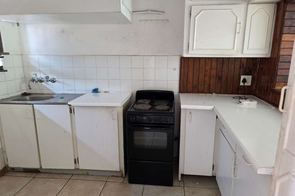 A dated kitchen featuring white cabinetry, tiled splashbacks, a stainless steel sink, and a freestanding electric stove.