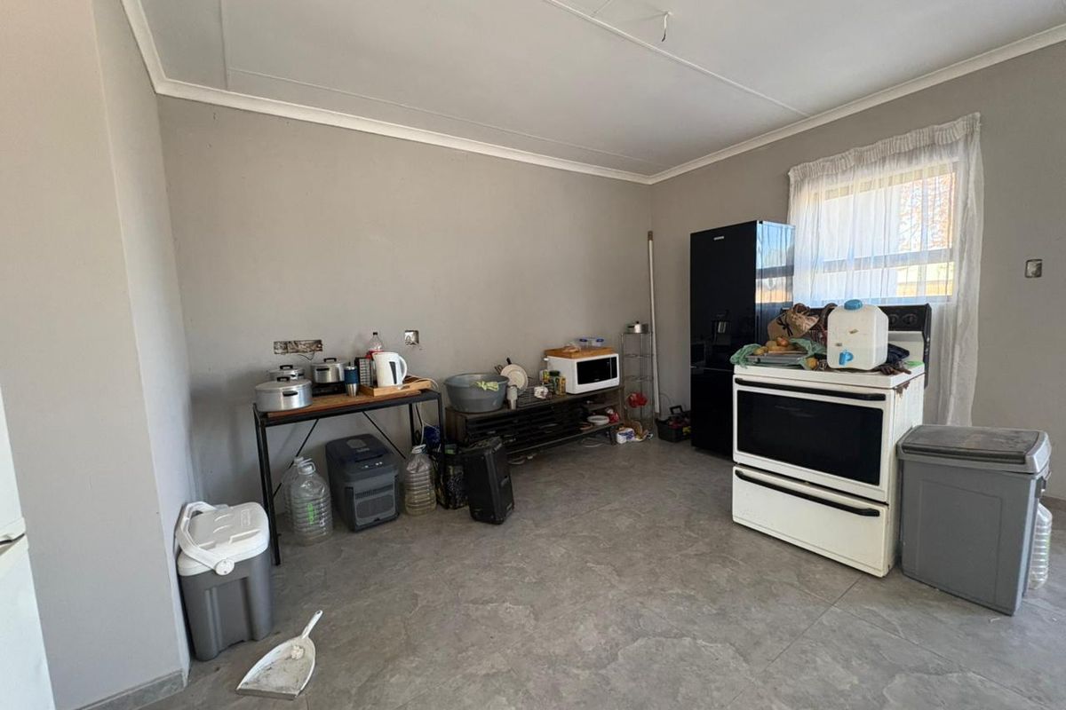 A functional kitchen area featuring tiled flooring, a freestanding stove, and basic utility space, currently lacking built-in cabinetry and finished fixtures.