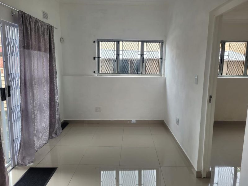 A bright, empty living area featuring neutral tiled flooring, security bars on windows, and a sliding door with a security gate.