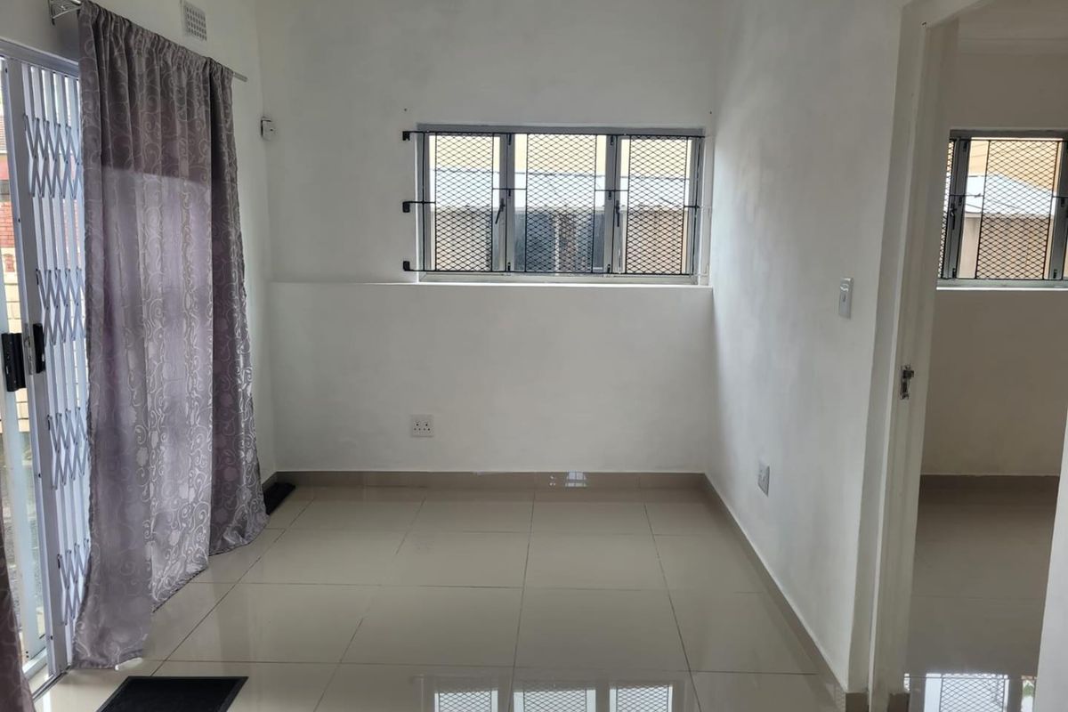 A bright, empty living area featuring neutral tiled flooring, security bars on windows, and a sliding door with a security gate.
