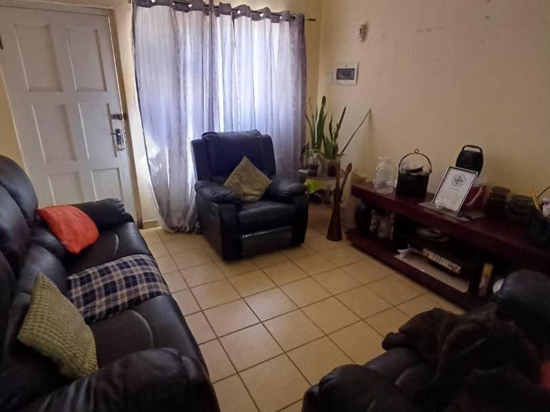 A living room featuring tiled flooring and a standard panel door, currently showing signs of wear on the wall surfaces.