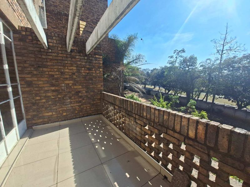 A spacious balcony featuring exposed brick walls, a decorative brick balustrade, and tiled flooring, offering an open outdoor area with a view.
