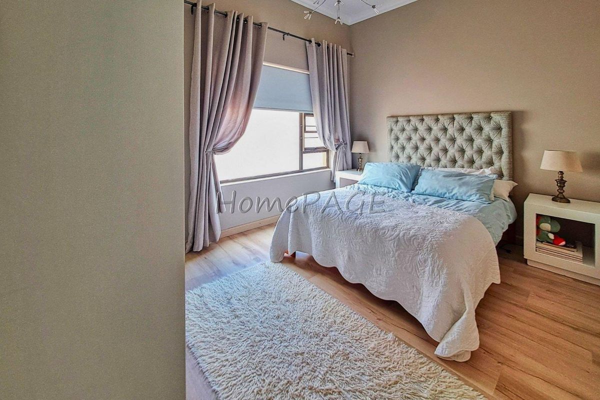 A well-maintained bedroom featuring light wood-look flooring, neutral wall tones, and a large window with integrated blinds and curtain tracks.