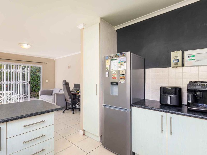 Open plan kitchen and living area featuring tiled flooring, laminate cabinetry, and direct access to the outdoor patio through a sliding security door.