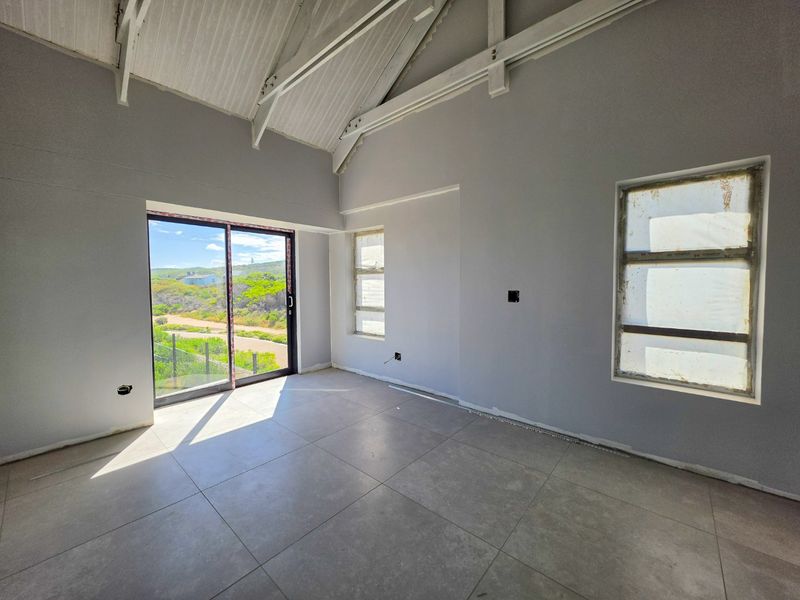 An empty, light-filled living area featuring a high vaulted ceiling with exposed timber trusses, large format floor tiles, and sliding doors leading outdoors.
