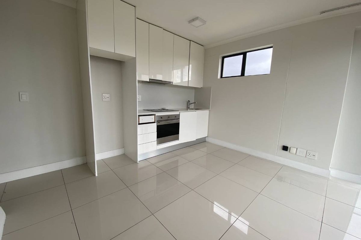 A modern, compact kitchen featuring high-gloss white cabinetry, integrated oven, hob, and extractor fan, complemented by neutral tiled flooring.