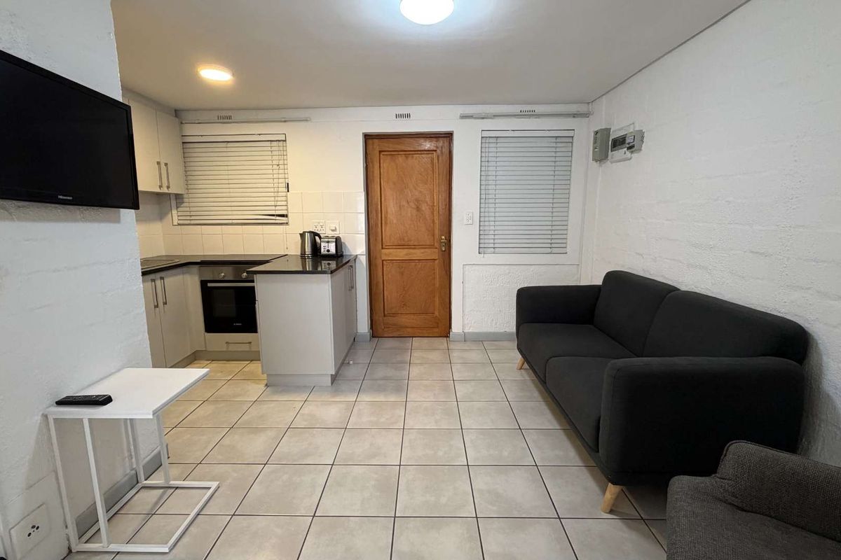 Open-plan living area featuring a compact kitchen with built-in cabinetry, oven, and hob, complemented by tiled flooring and neutral wall finishes.