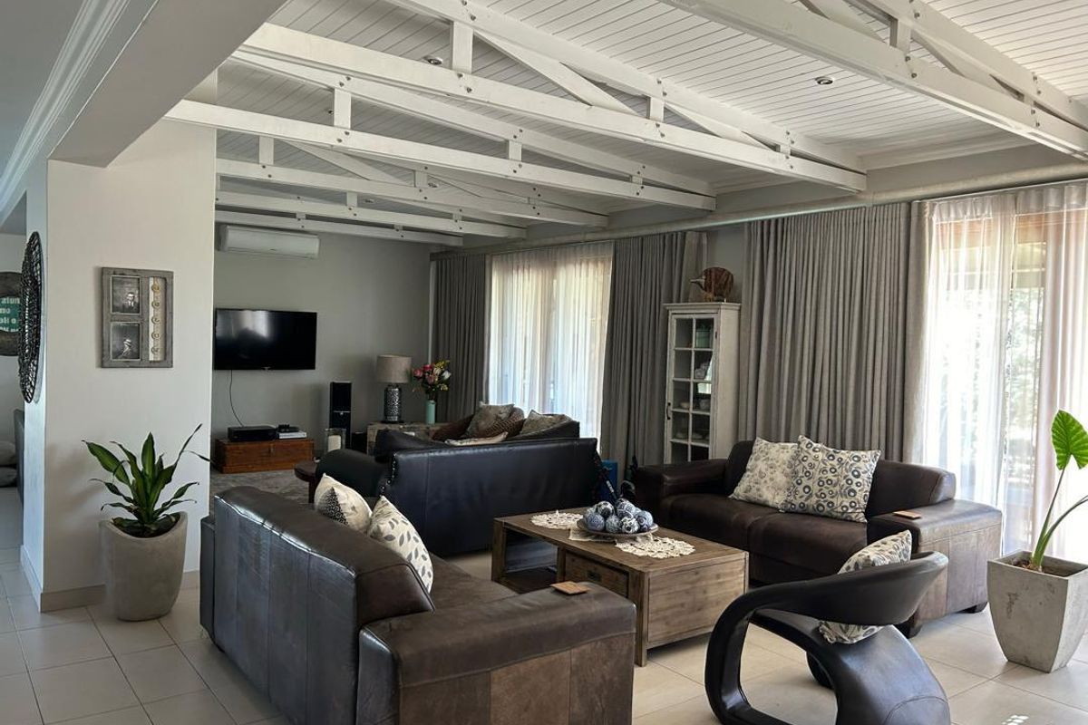Spacious living room featuring high vaulted ceilings with exposed white timber trusses, tiled flooring, and large glass doors leading to the outdoor area.