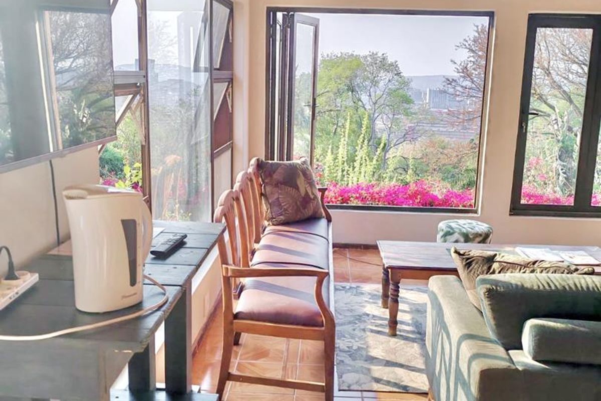 A bright living area featuring timber ceilings, tiled floors, and large windows that provide ample natural light and scenic outdoor views.