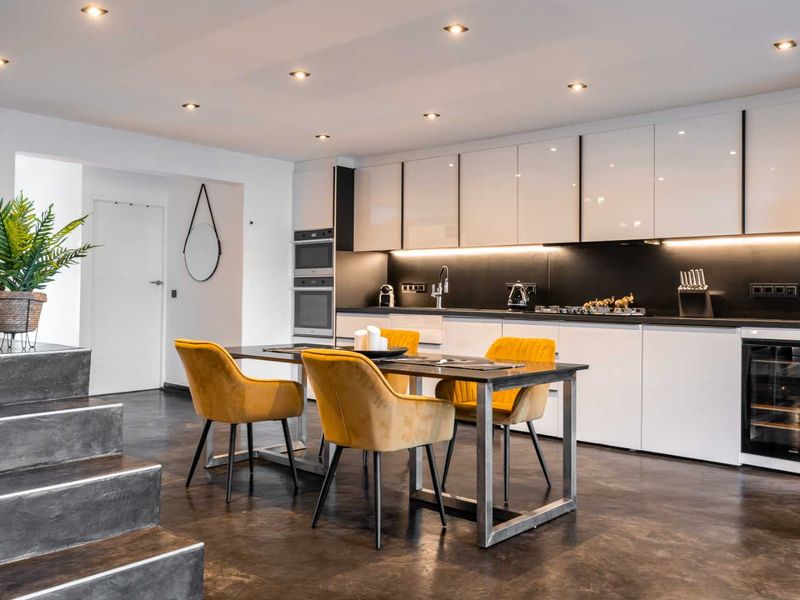 Modern open-plan kitchen featuring sleek white cabinetry, integrated appliances, recessed lighting, and a contemporary dark floor finish.