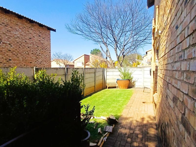 A private rear garden area featuring a brick-paved walkway, a small lawn, and enclosed by precast concrete boundary walls.