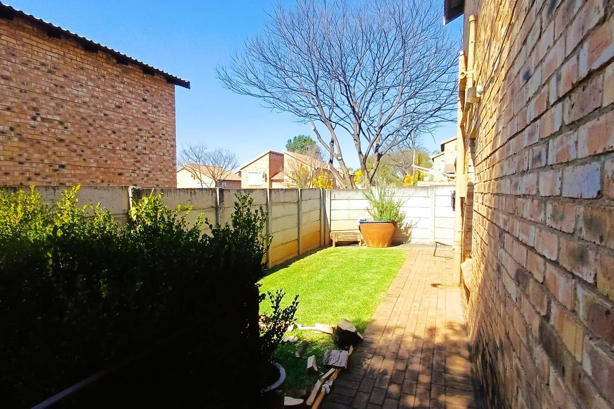 A private rear garden area featuring a brick-paved walkway, a small lawn, and enclosed by precast concrete boundary walls.