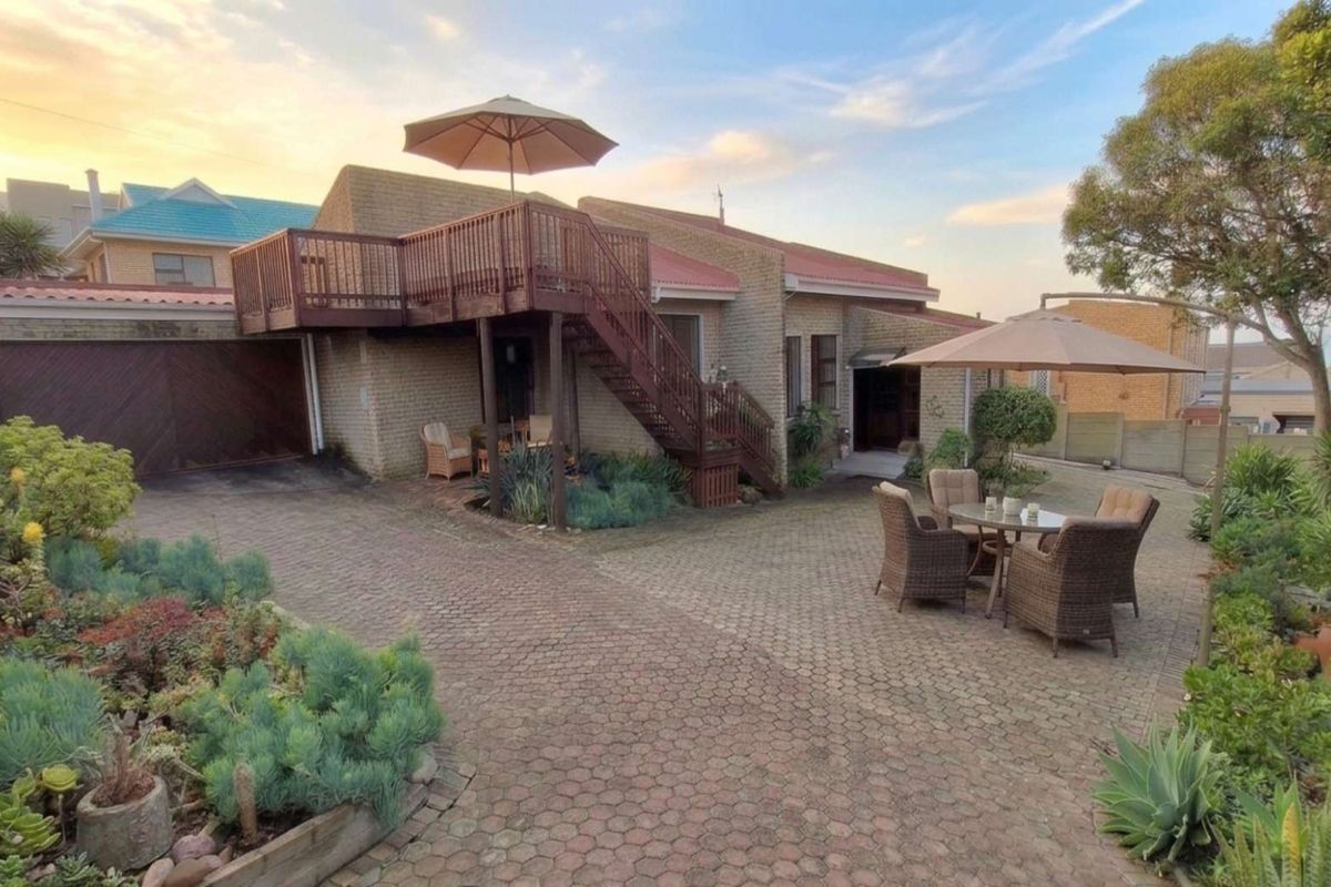 Rear exterior view featuring a paved courtyard, raised timber deck with staircase, and established garden landscaping.