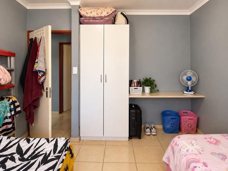 A bedroom featuring tiled flooring, a built-in wardrobe, and a fixed desk area with neutral wall finishes.