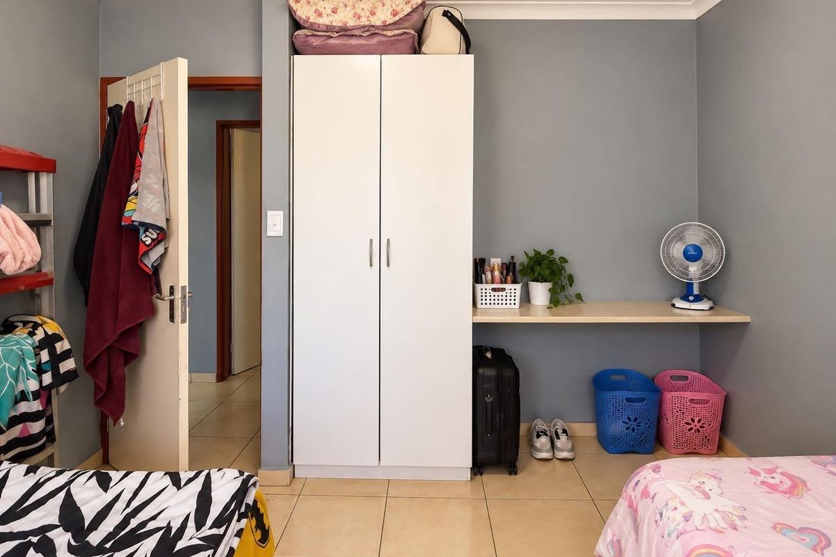 A bedroom featuring tiled flooring, a built-in wardrobe, and a fixed desk area with neutral wall finishes.