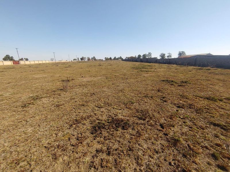 A wide-angle view of a vacant agricultural plot featuring dry grass and perimeter boundary walls.