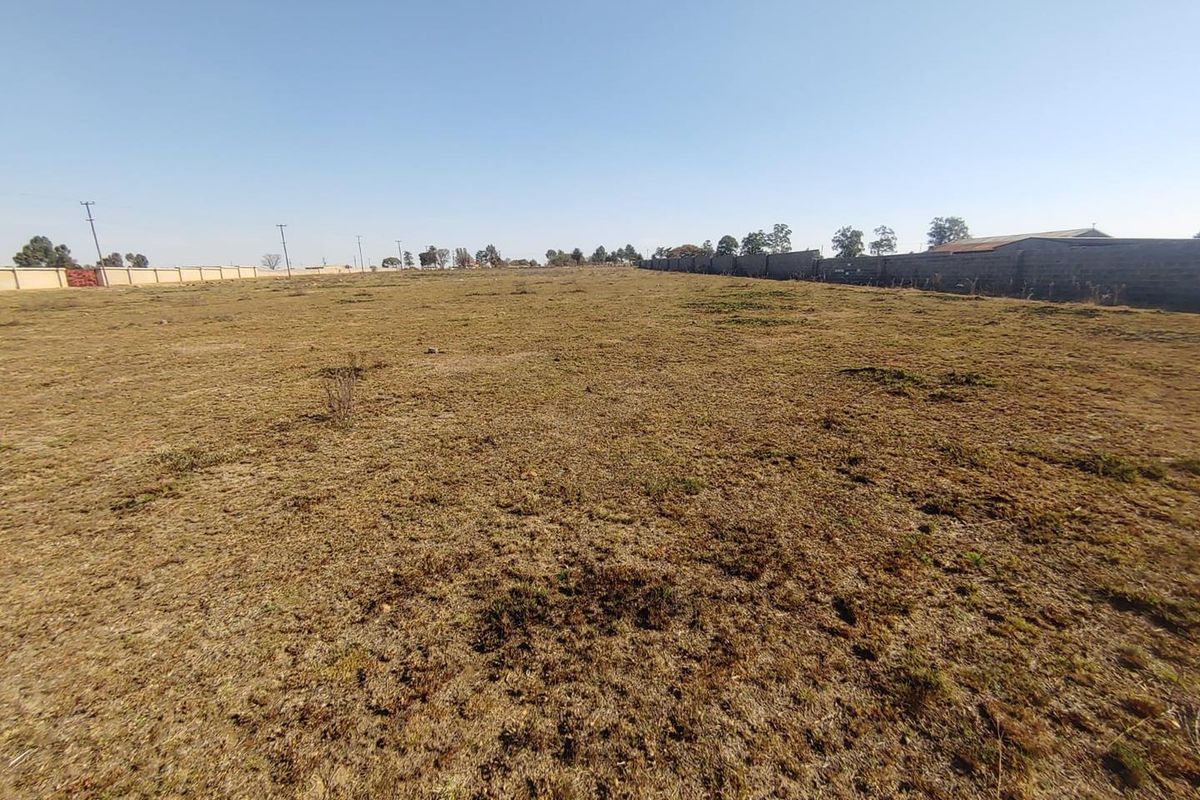 A wide-angle view of a vacant agricultural plot featuring dry grass and perimeter boundary walls.