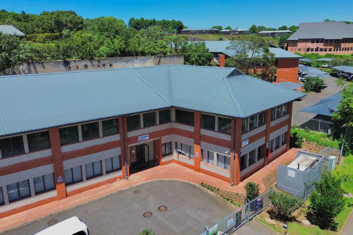 Aerial view of a two-story brick office building featuring a metal roof, paved driveway, and secure perimeter fencing within a landscaped office park.