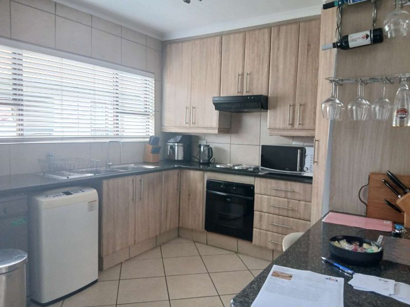 A functional kitchen featuring light wood-tone cabinetry, dark granite countertops, built-in oven, extractor fan, and tiled flooring with a large window.