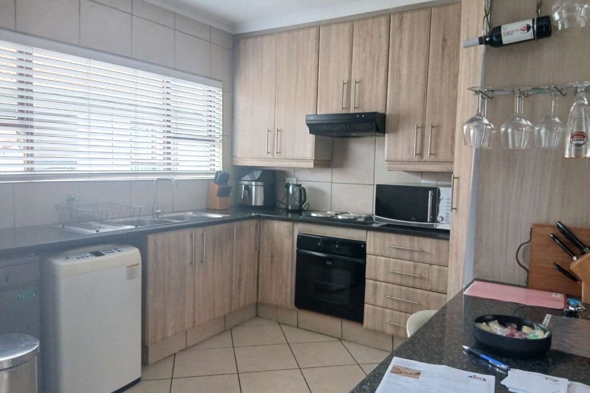 A functional kitchen featuring light wood-tone cabinetry, dark granite countertops, built-in oven, extractor fan, and tiled flooring with a large window.