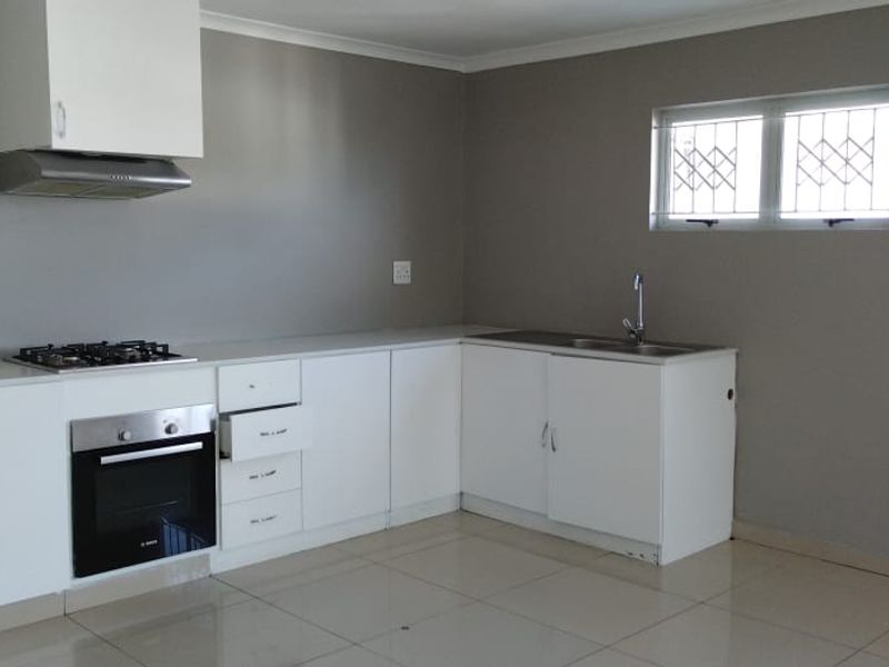 A clean, empty kitchen featuring white cabinetry, a gas hob, built-in oven, extractor fan, and tiled flooring, ready for personalization.